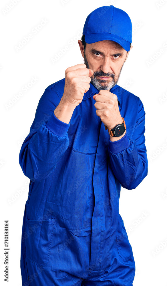 Middle age handsome man wearing mechanic uniform ready to fight with fist defense gesture, angry and upset face, afraid of problem Middle age handsome man wearing mechanic uniform ready to fight with fist defense gesture, angry and upset face, afraid of problem
