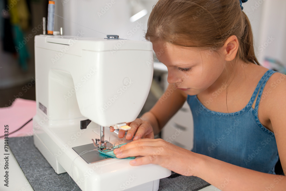 Little girl using a sewing machine to sew on a piece of fabric. Creative tailoring workshops for children - concept Little girl using a sewing machine to sew on a piece of fabric. Creative tailoring workshops for children - concept