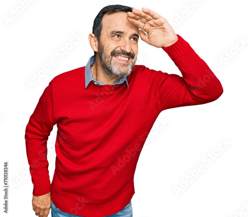 Middle age hispanic man wearing casual clothes very happy and smiling looking far away with hand over head. searching concept.