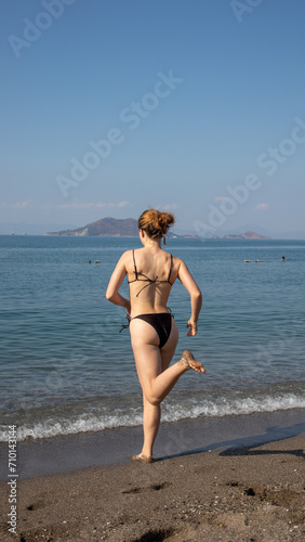 Fit young woman in bikini running out towards the sea at the beach, in Fethiye, Turkey
