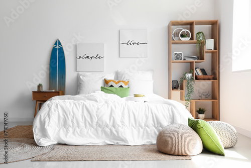 Cozy bed with white blanket and surfing board in interior of stylish bedroom