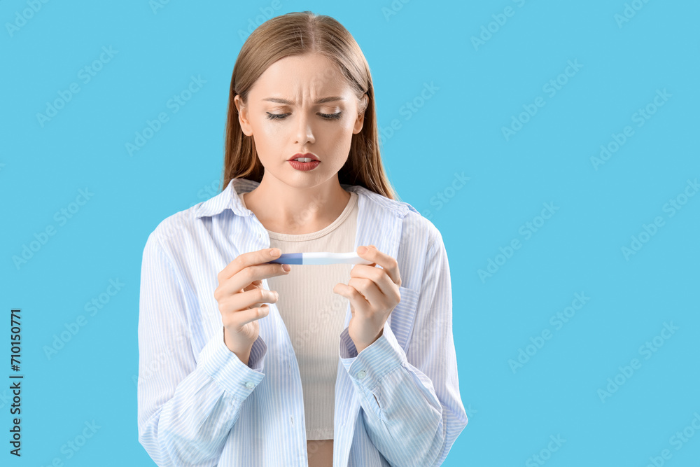 Worried young woman with pregnancy test on blue background Worried young woman with pregnancy test on blue background