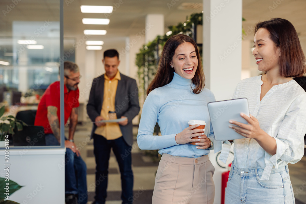 Two diverse business woman chatting in an office and using a tablet Two diverse business woman chatting in an office and using a tablet