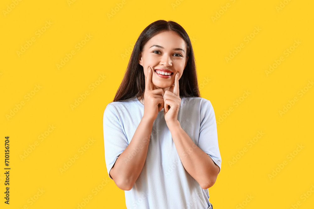 Smiling young Asian woman with healthy teeth on yellow background - obrazy, fototapety, plakaty 