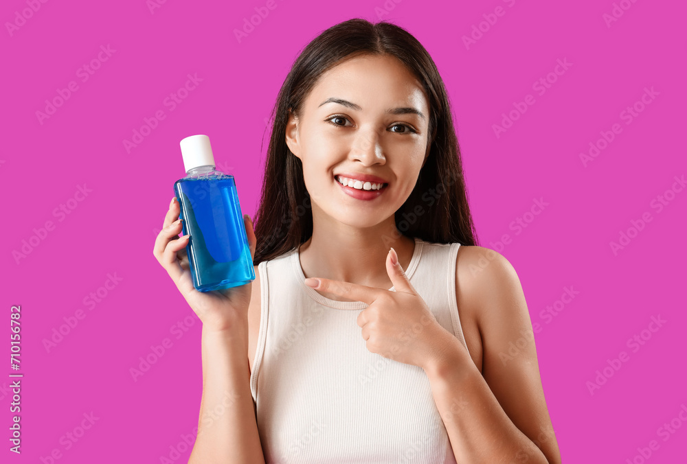 Smiling young Asian woman pointing at mouth rinse on purple background Smiling young Asian woman pointing at mouth rinse on purple background