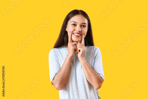Smiling young Asian woman with healthy teeth on yellow background