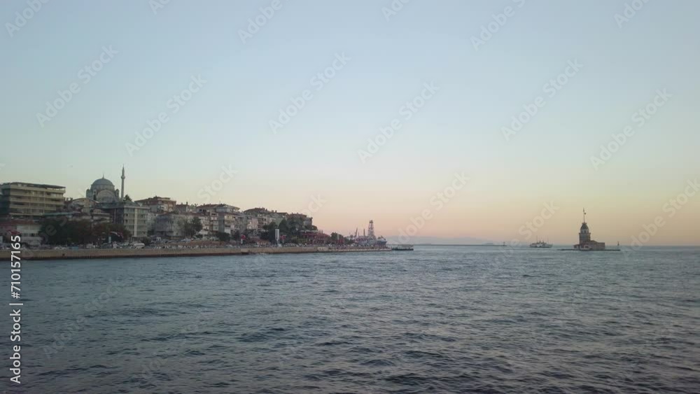 Evening, cinematic slow-mo, the view of uskudar and the adjacent Maiden's Tower (Kiz Kulesi) from a ferry sailing along the Istanbul Bosphorus. Golden hour, with a harbor visible in the background. Evening, cinematic slow-mo, the view of uskudar and the adjacent Maiden's Tower (Kiz Kulesi) from a ferry sailing along the Istanbul Bosphorus. Golden hour, with a harbor visible in the background.