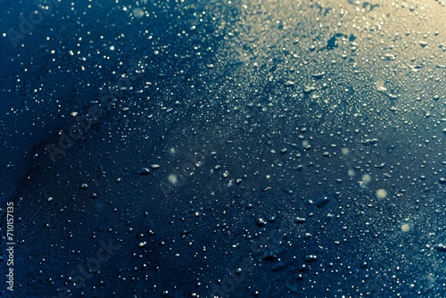 Close-up of water droplets on a dark blue surface with highlights and reflections, creating a fresh and clean feeling.