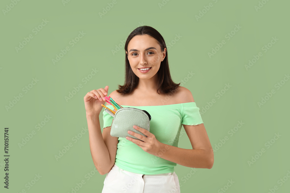 Beautiful young woman with cosmetic bag full of makeup products on green background Beautiful young woman with cosmetic bag full of makeup products on green background