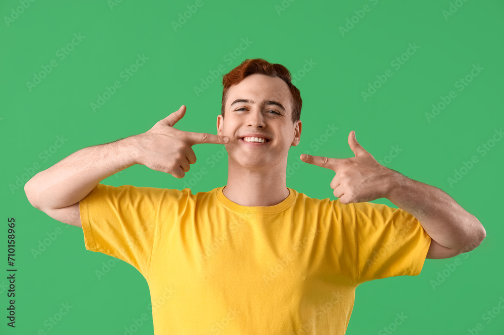 Fototapeta premium Young man pointing at his teeth on green background, closeup