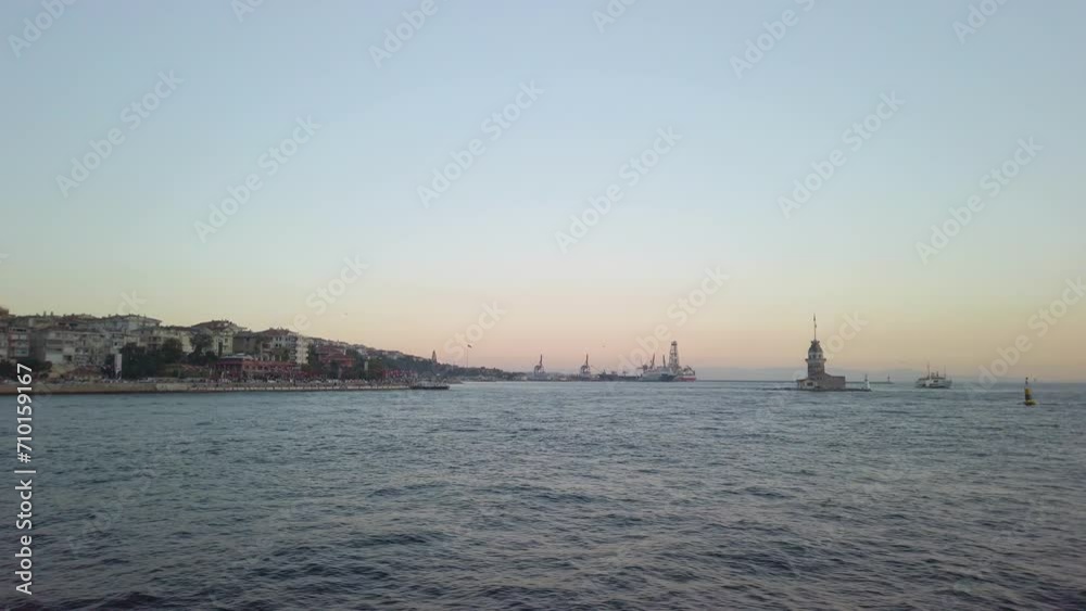 Evening, cinematic slow-mo, the view of uskudar and the adjacent Maiden's Tower (Kiz Kulesi) from a ferry sailing along the Istanbul Bosphorus. Golden hour, with a harbor visible in the background. Evening, cinematic slow-mo, the view of uskudar and the adjacent Maiden's Tower (Kiz Kulesi) from a ferry sailing along the Istanbul Bosphorus. Golden hour, with a harbor visible in the background.
