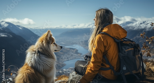 Cinematic image of a hiker girl with her dog at the top of the mountain with rocks, autumn trees and lake. Long shot of a beautiful scene in autumn from the top. © Loucine