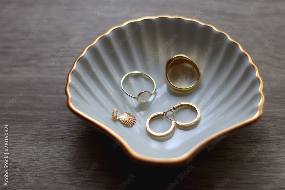 Ring dish shaped like a seashell with gold rings, earrings and pendant. Wooden background, selective focus.