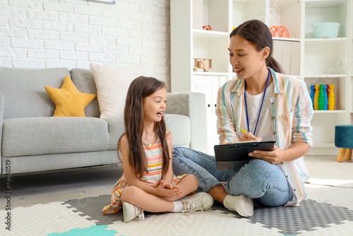 Female Asian speech therapist writing on clipboard and little girl in office photo