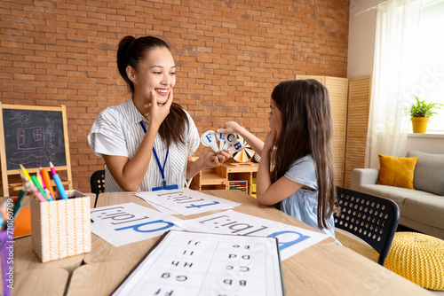 Female Asian speech therapist teaching little girl how to pronounce letters in office photo