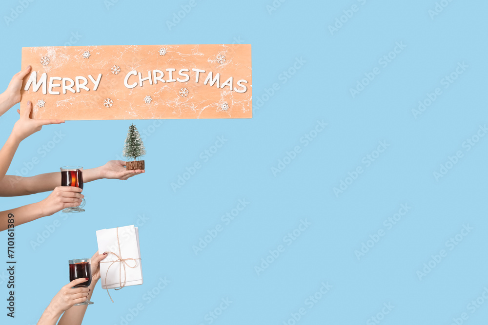 Female hands with glasses of warm mulled wine and Christmas decor on blue background Female hands with glasses of warm mulled wine and Christmas decor on blue background