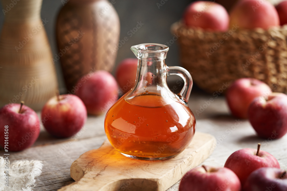 A glass jug of apple cider vinegar with fresh apples on a table A glass jug of apple cider vinegar with fresh apples on a table