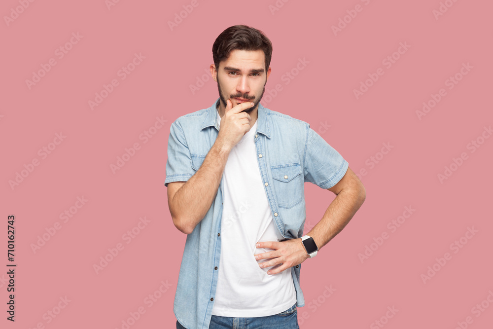 Portrait of thoughtful handsome bearded man in blue casual style shirt standing with pensive expression, trying to remember something. Indoor studio shot isolated on pink background. Portrait of thoughtful handsome bearded man in blue casual style shirt standing with pensive expression, trying to remember something. Indoor studio shot isolated on pink background.