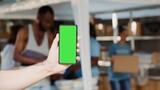 Focus on a male hand vertically holding mobile phone displaying isolated chromakey template at outdoor food bank. Close-up of caucasian person grasping cellphone with green screen.