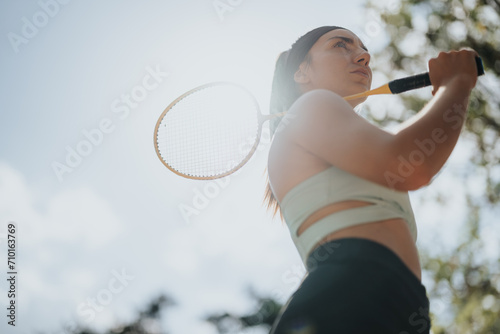 A sports, female person is holding a racket on her shoulder. Low angle view photo. Copy space. © qunica.com