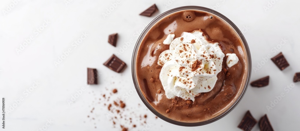 Top view of a white background with a glass cup of tasty hot chocolate topped with whipped cream.