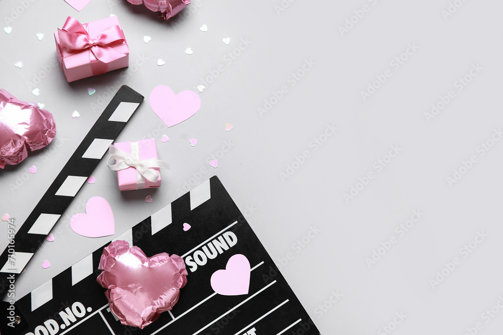 Obraz premium Movie clapper with heart shaped air balloons and gift boxes on grey background. Valentine's Day celebration