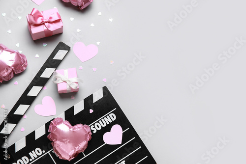 Movie clapper with heart shaped air balloons and gift boxes on grey background. Valentine's Day celebration