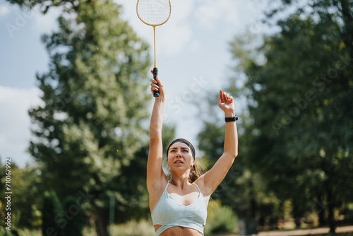 Fit woman playing badminton in a sunny park. Enjoying outdoor exercise and friendly competition in a natural environment. © qunica.com
