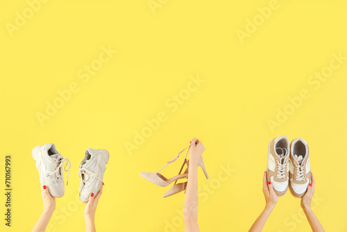 Female hands holding different shoes on yellow background photo