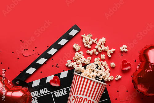 Movie clapper with bucket of popcorn and heart shaped decor on red background. Valentine's Day celebration