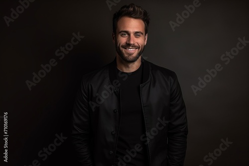 Portrait of a handsome young man in a black jacket on a dark background.