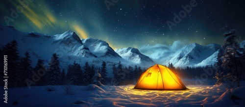Winter field with a yellow tent illuminated from within, surrounded by a breathtaking starry sky and the Northern lights. Spectacular nocturnal scene. photo