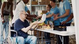 The needy are helped and fed by charitable group, and homeless people are given free food, including fresh fruit. Wheelchair-bound disabled man is given a warm meal from volunteer at a food drive.