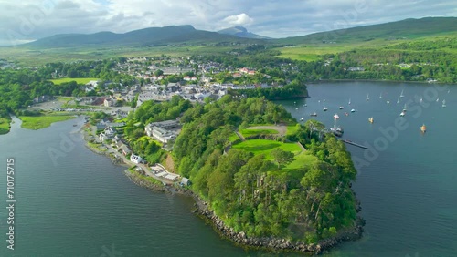 AERIAL: Picturesque seaside town with harbour on the Isle of Skye on a sunny day. Charming Portree in a sheltered part of the coast of a hilly and green island. Beautiful scenery in northern Scotland. photo