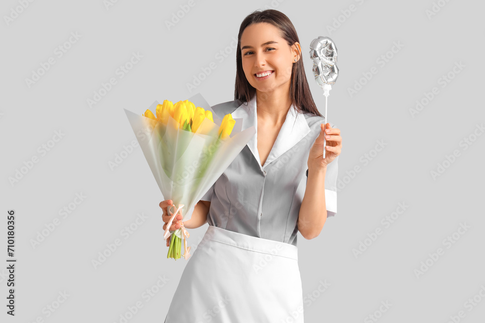 Young chambermaid with bouquet of tulips and figure 8 on light background. International Women's Day Young chambermaid with bouquet of tulips and figure 8 on light background. International Women's Day