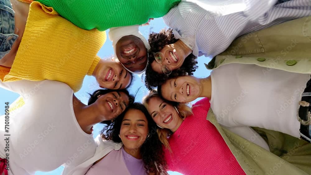 Low angle view of diverse group of young women standing together in circle, hugging each other while smiling at camera. Female friendship and community, feminism and unity concept.