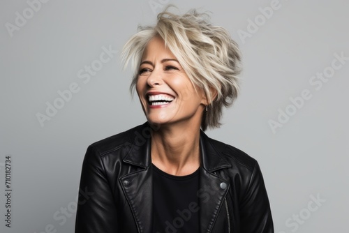 Portrait of a happy mature woman in black leather jacket laughing against grey background