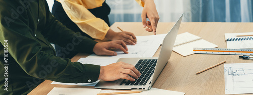 Professional architect edited blueprint by using laptop while project manager point the mistake point at meeting room on meeting table with architectural document scatter around. Closeup. Delineation.