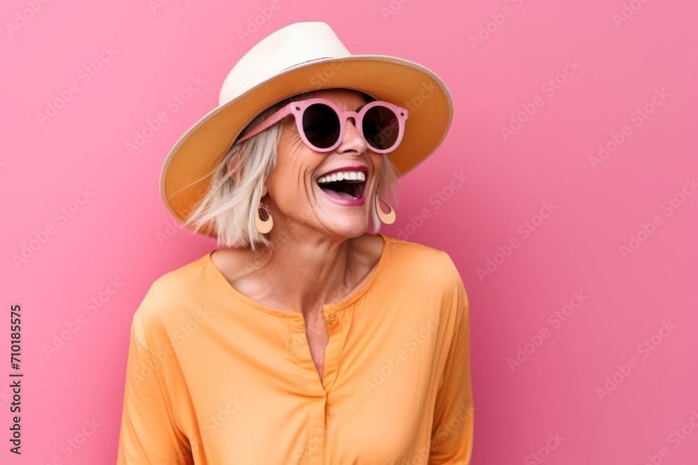 Portrait of a happy woman in sunglasses and hat over pink background
