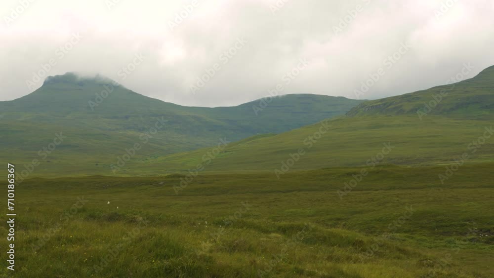 Beautiful hilly landscape covered with vivid green grass on a cloudy summer day. A picturesque and dramatic scenery with constantly changing weather on a green Isle of Skye in the north of Scotland. Beautiful hilly landscape covered with vivid green grass on a cloudy summer day. A picturesque and dramatic scenery with constantly changing weather on a green Isle of Skye in the north of Scotland.