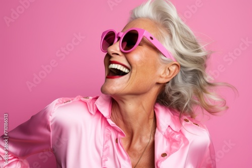 Portrait of happy senior woman in sunglasses, over pink background. © Iigo