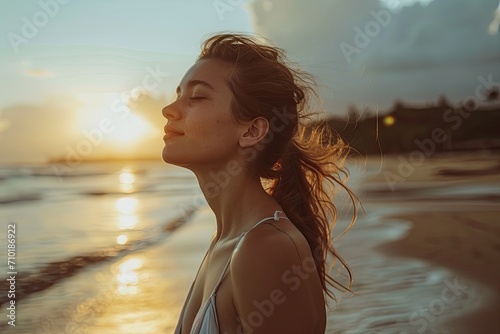A peaceful woman embraces the beauty of nature as the sun sets behind her on a summer beach, her eyes closed in serene bliss © AiAgency