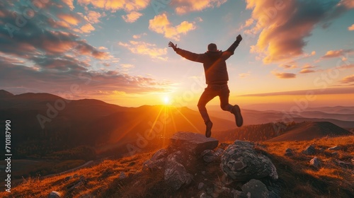 Victory jump of a young guy on a mountaintop at sunrise. He is celebrating as he reaches the top when first rays of autumn morning sun start spilling over the alpine hilltop.