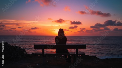 Wide angle shot of the Silhouette of a woman sitting on a bench looking at the tranquil sunset over the ocean