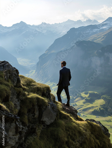 Ein Businessmann steht auf einem Berg in den Schweizer Alpen und schaut zuversichtlich in die Landschaft