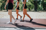 Fit girls training outdoors, jogging on a race track in a city park. Active and happy, promoting a healthy lifestyle.