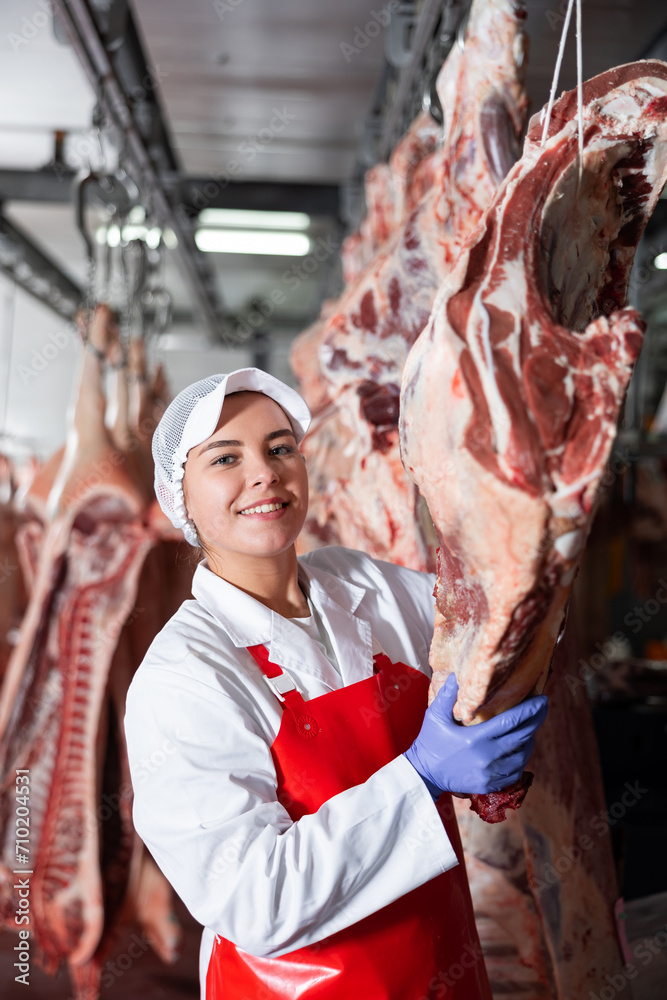 Female butcher in slaughterhouse showing piece of cow carcass