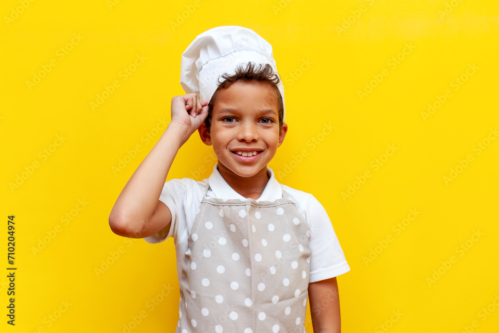 african american boy in uniform and chef's hat smiling on yellow isolated background, teenager child in apron looking at camera african american boy in uniform and chef's hat smiling on yellow isolated background, teenager child in apron looking at camera