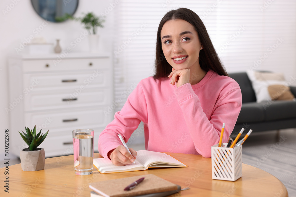 Young woman writing in notebook at wooden table indoors Young woman writing in notebook at wooden table indoors