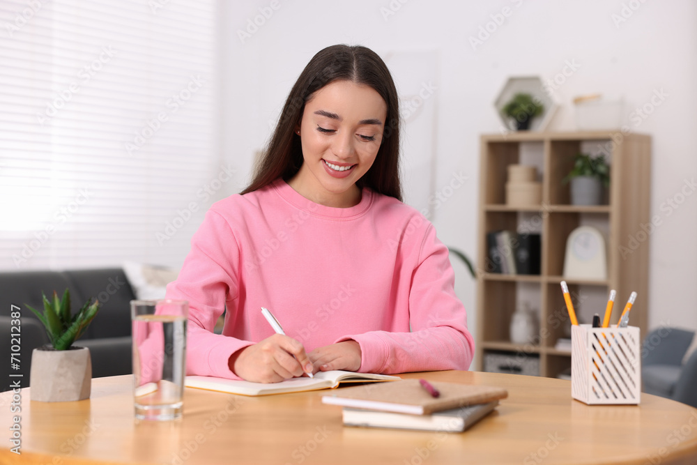 Young woman writing in notebook at wooden table indoors Young woman writing in notebook at wooden table indoors